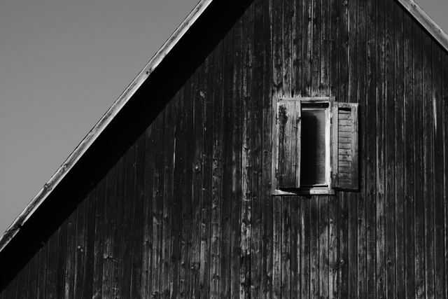A weathered black and white wooden barn wall with a small window