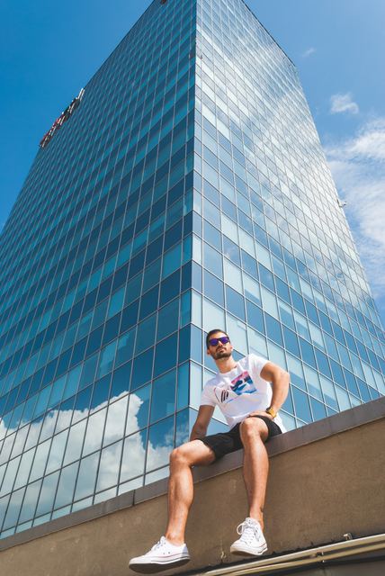 A man sitting on a ledge in front of a blue glass skyscraper